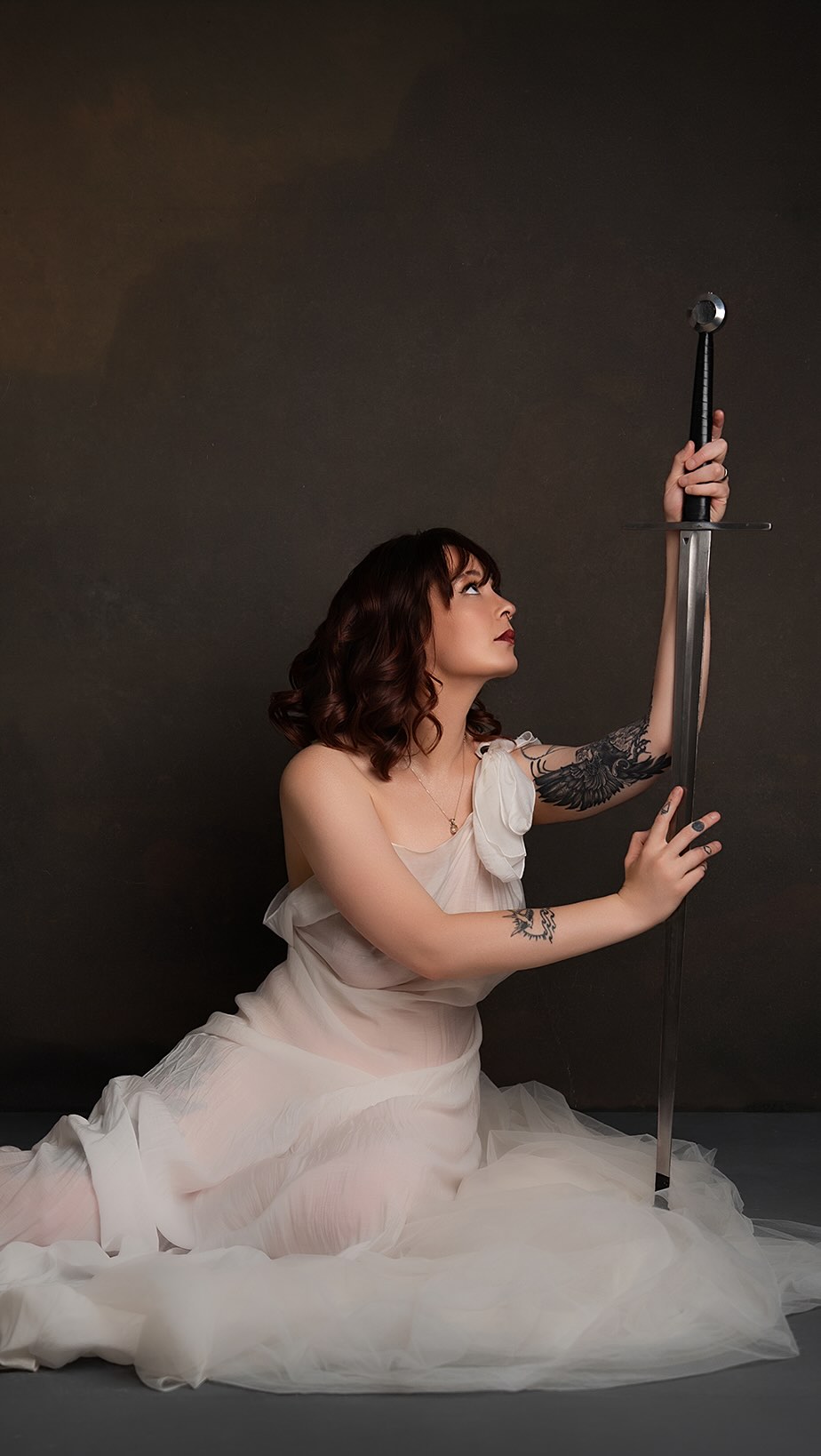 Romantasy inspired boudoir portrait of a woman in ivory tulle holding a sword in a candlelit studio